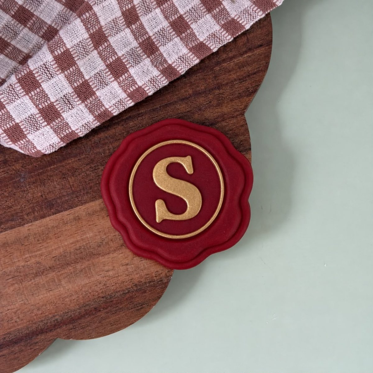 Rood lakzegel koekje met een gouden S op een houten plank